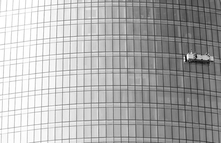 gallery-02 High-rise window washers in safety gear cleaning a skyscraper facade.
